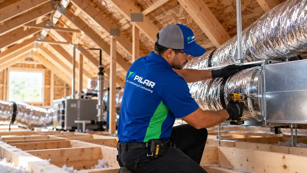 A Pilar Services technician in an attic clamping an insulated flexible duct to a sheet-metal plenum