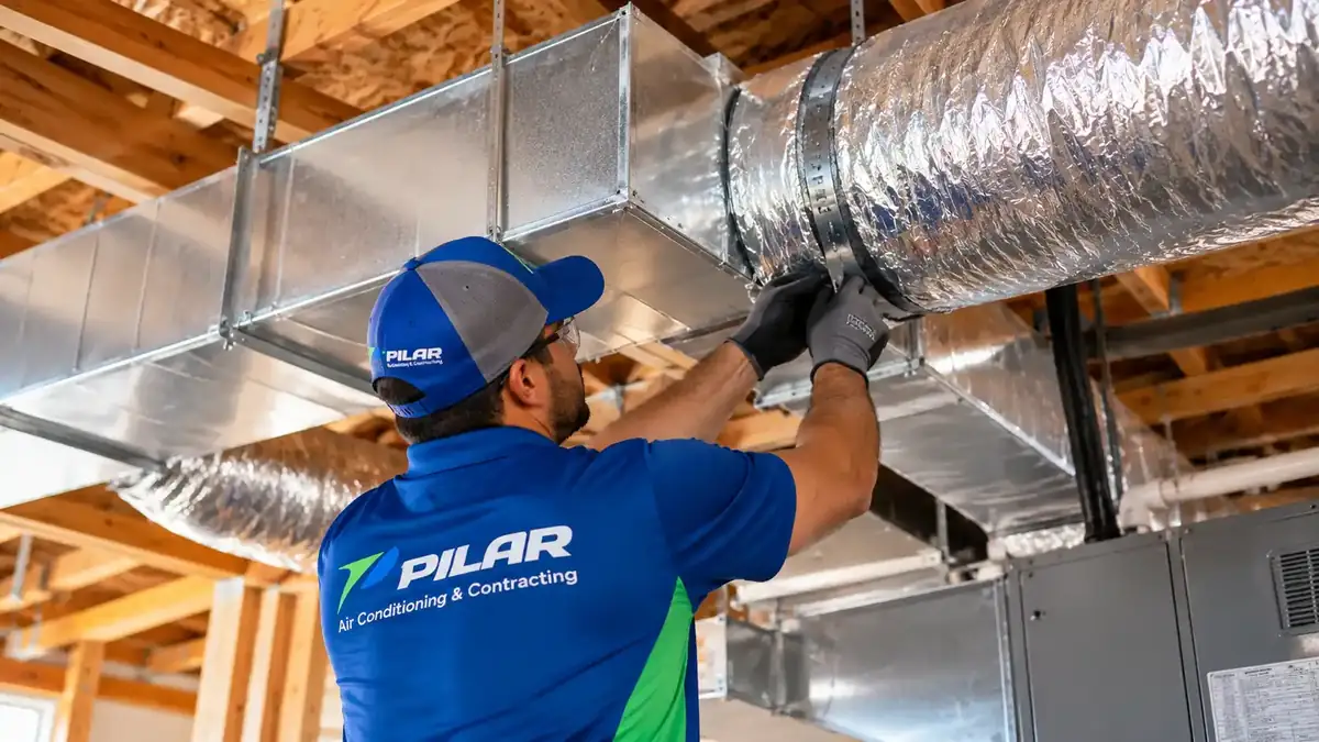 A Pilar Services technician joining an insulated flexible duct to rectangular ductwork overhead