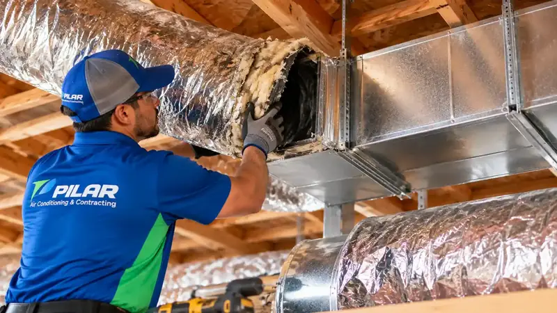A Pilar Services technician pulling a worn, frayed insulated duct off a sheet-metal trunk line