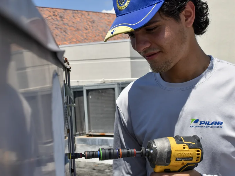 Pilar Services technician driving screws into an air handler panel with a cordless impact driver