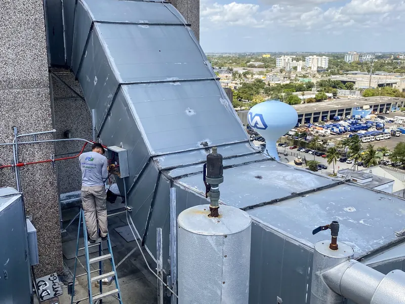 Pilar Services technician on a ladder servicing rooftop duct work on a high-rise building
