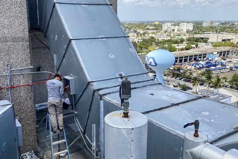 Pilar Services technician on a ladder servicing rooftop duct work high above a Florida city