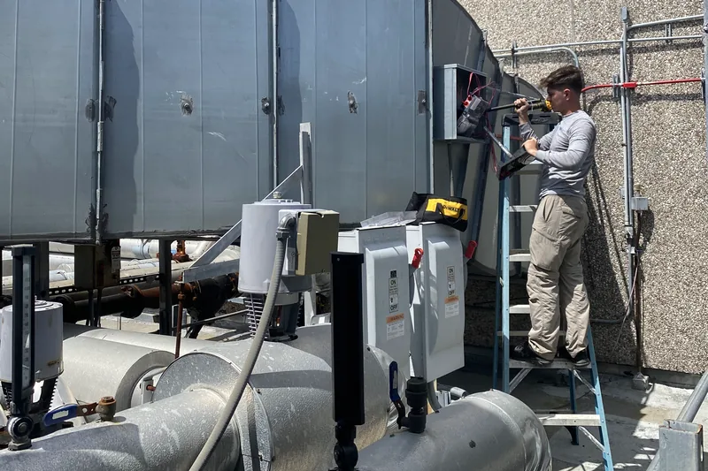 Pilar Services technician on a ladder servicing a commercial rooftop air handler