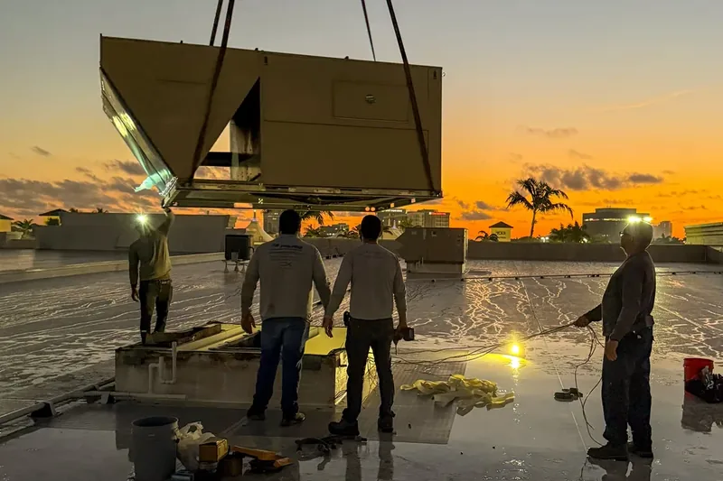 Crane lowering a new rooftop package unit into place on a Florida commercial roof at dusk